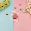 Detail of red apple resin pendant charm packaged in a transparent serrated plastic bag - Red Apple