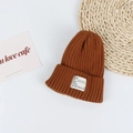 Detail of caramel brown ribbed knit beanie with a white rectangular decorative logo tag - Head Circumference 50-58cm / Caramel color