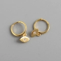 Detail of gold eye-shaped charm earrings with inlaid zircon crystal on gray background - Gold