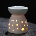 White ceramic aromatherapy lamp with star cutouts glowing warmly on wooden surface - Gypsophila Geometric / Aromatherapy Burner + Candle Tray