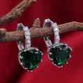 Macro shot of green heart-shaped crystal earrings hanging on a rustic wood branch - Emerald
