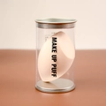 Macro shot of a peach-colored makeup puff in a clear plastic tube with metal lid - Beveled Shape (Cylinder Pack) / Nude