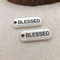 Silver rectangle charms with 'BLESSED' engraving on rustic beige linen fabric background - Blessed
