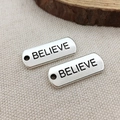 Silver rectangular metal charms with BELIEVE engraving on beige linen fabric background - Believe