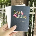 Hand holding a black textured Best Wishes greeting card with 3D floral paper cutouts - S-Style Best Wishes