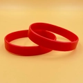 Set of two minimalist red silicone wristbands displayed on a solid yellow background - Red