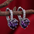 Detailed shot of silver heart earrings with purple crystals on a velvet background - Purple