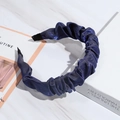 Detail of blue pleated fabric headband with shiny satin texture on a white book base - Blue