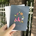 Dark grey greeting card with pink paper-cut birds and gold foil text held in hand - S-Style Bird