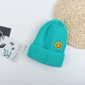 Detail der petrolfarbenen Strickmütze mit gelber Smiley-Stickerei auf einer Flechtmatte - M (56-58cm) / See Blau