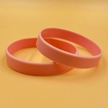 Pair of soft pink silicone wristbands presented on a clean warm orange background - Pink