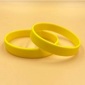 Pair of blank yellow silicone wristbands displayed on a solid clean orange background - Yellow