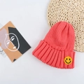 Close-up of coral pink knitted beanie with a yellow smiling face embroidery patch - 50-56cm / Watermelon red