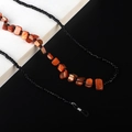 Detalle de cadena para gafas con conchas naranjas y cuentas negras sobre fondo bicolor - Naranja