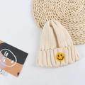 Close-up of off-white knit beanie featuring a yellow smiley face patch on a woven mat - 50-56cm / Off-white
