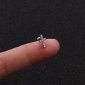 Dettaglio di un piccolo orecchino a croce d'argento con zirconi tenuto tra le dita - Stile Croce (1#)
