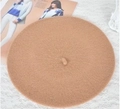 Detailed top view of a classic camel wool beret hat placed on decorative lace and a magazine - M / Camel