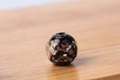 Einzelne schwarze Leuchtglasperle mit Goldsandeinschlüssen auf Holzoberfläche - 6mm / Transparent Schwarz
