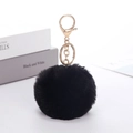 Black faux rabbit fur ball keychain with golden metal ring on minimalist background - Black