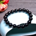 Macro shot of polished black agate beads on a blue ceramic base with a dark wood background - 10MM Natural Black Agate