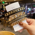 Detailed view of four golden chain hair clips with black acrylic accents on card - Style E