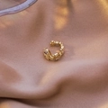 Vue macro d'un ear cuff doré avec zircons sur un tissu en soie rose élégant - Style Goutte d'Eau