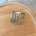 Detail eines silbernen Haarkamms mit 10 gewellten Zähnen auf einem Holztablett - Metalllegierung / Silber
