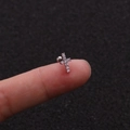 Dettaglio di un piccolo orecchino a croce d'argento con zirconi tenuto tra le dita - Stile Croce (1#)