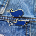 Enamel pins featuring whale and shark designs with gold trim on denim fabric - Shark And Whale