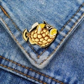 Detailopname van een emaille visspeld met gele patronen op blauwe denim stof - Luipaardtrekkervis
