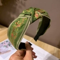 Close-up of green silk fabric headband with colorful floral embroidery and center knot - Green