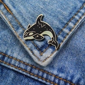 Detailed view of an orca enamel pin with gold constellations on blue denim fabric - Starry Orca