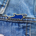 Primer plano de un broche de tiburón en esmalte azul oscuro con bordes dorados en denim - Tiburón azul marino