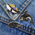 Three enamel whale brooches with moon and star patterns pinned on blue denim pocket - Whale Combo