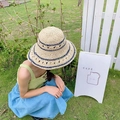 Dettaglio ravvicinato di cappello di paglia intrecciata con strisce blu e fiori - Regolabile / Beige
