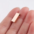 Close-up van een kleine goudkleurige rechthoekige metalen hanger op een vingertop geplaatst - Roségoud