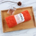 Close-up of a soft orange coral fleece towel with Joy Life sleeve on a wooden tray - 35*75cm / Watermelon red