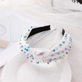 White knotted headband with colorful beads on a white plate with soft lighting - White