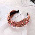 Pink fabric headband with knotted design and colorful pearls on white ceramic plate - Rust Red