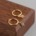 Macro shot of gold S925 sterling silver hoop earrings with diamond-set rhombus charms - Gold