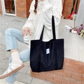 Detail view of large black canvas tote bag with white patch label and wide shoulder straps - Black