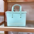 Detailed view of mint green PVC tote bag with pyramid studs on a golden shelf - Small / Light Green
