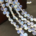 Close-up of heart-shaped opal beads for DIY jewelry making hanging over a wooden box - 10mmx12mm / Opal