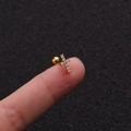 Makroaufnahme von 16G Gold Kreuz-Ohrknorpel-Ohrring mit Zirkonia auf den Fingerspitzen - Kreuzstil Gold (No.13 Gold) / 1.2x6mm (Stabdicke x Länge)