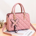 Pink quilted shoulder bag with bow charm and gold hardware on a wooden surface - Pink