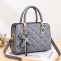 Bolso de mano gris acolchado con herrajes dorados y colgante de mariposa sobre madera - Gris claro