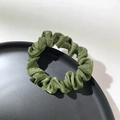 Close-up of olive green satin scrunchie with elegant folds on black tray background - Green
