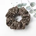 Close-up of dark brown floral scrunchie with white flower print on soft fabric texture - Coffee Bellflower