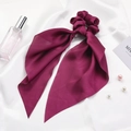 Detail of burgundy satin silk scrunchie with long ribbon on elegant white fabric - Burgundy