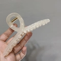 Detail showing high-quality large hair claw clip in jelly cream resin held against a wall - Apricot